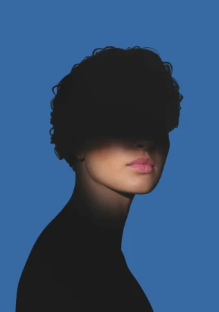 Close-up portrait of a woman with short dark curly hair and pink lipstick against a solid blue background.