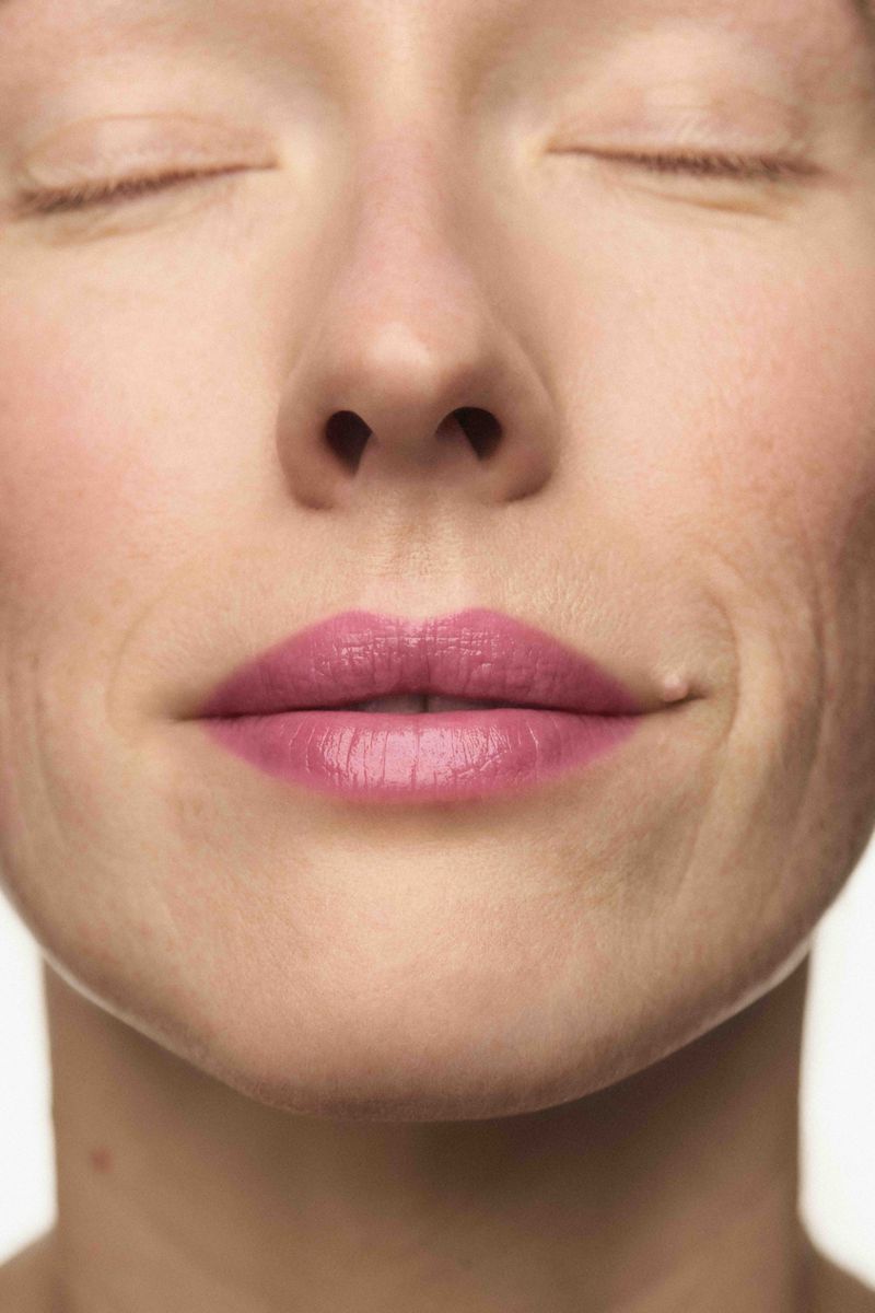 Close-up beauty portrait of a person with eyes closed wearing pink lipstick against a seamless background