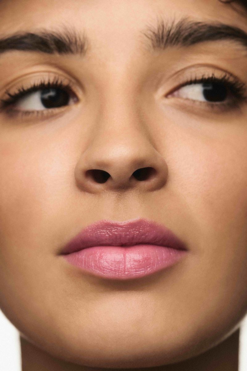 Close-up portrait of a woman showing glossy pink lipstick and natural makeup for a beauty campaign.