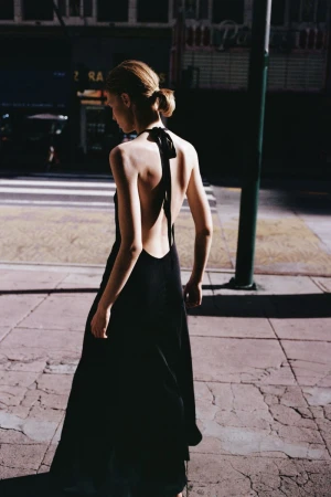 Model with hair in a low bun wearing a black halter dress walking on a city street.