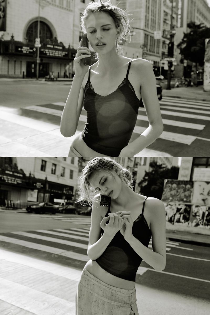 Model wearing a black camisole top standing on a city street holding a mobile phone to her ear.