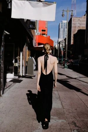 Model walking away on a sunny city sidewalk wearing a black halter dress with a low back for Zara