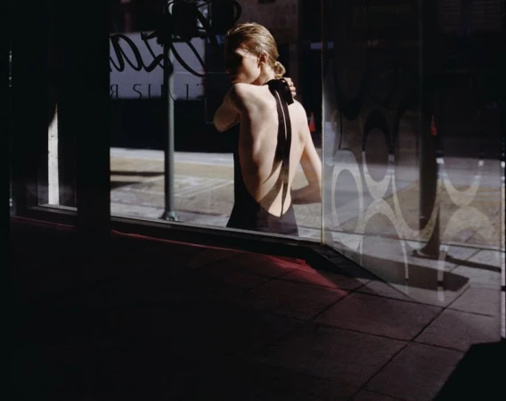 Model in a black backless halter dress viewed through a storefront window with graphic circular patterns.