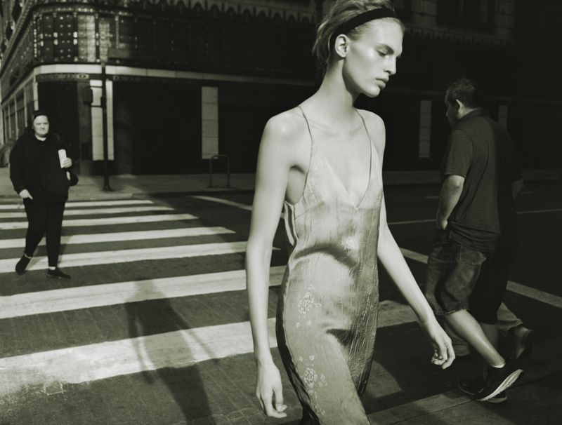 Model wearing a slip dress walking across a city street with pedestrians in the background