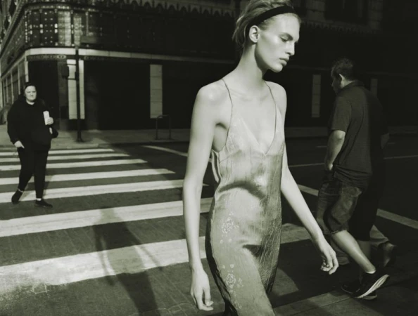 Model wearing a slip dress walking across a city street with pedestrians in the background