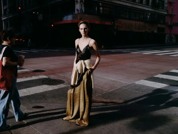 Model standing on a city street wearing a black top and long metallic skirt with a sweater tied around her waist.