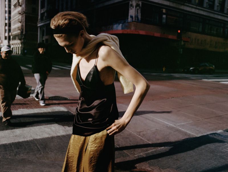 Model in a black satin top and gold skirt walking down an urban street for Zara