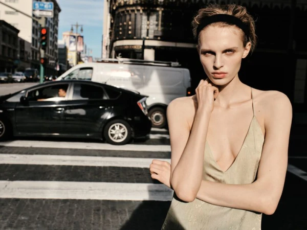 Model wearing a light dress and headband posing on a city street with cars and traffic light in the background.