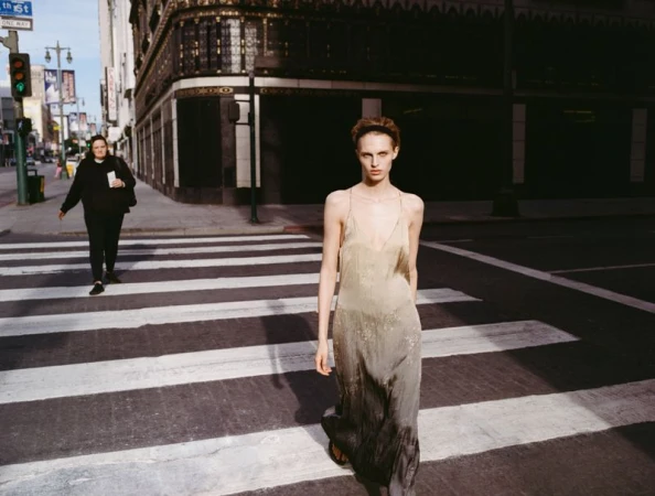 Model walking across a city crosswalk wearing a long gradient slip dress in a Zara campaign photographed by Sonia Szostak