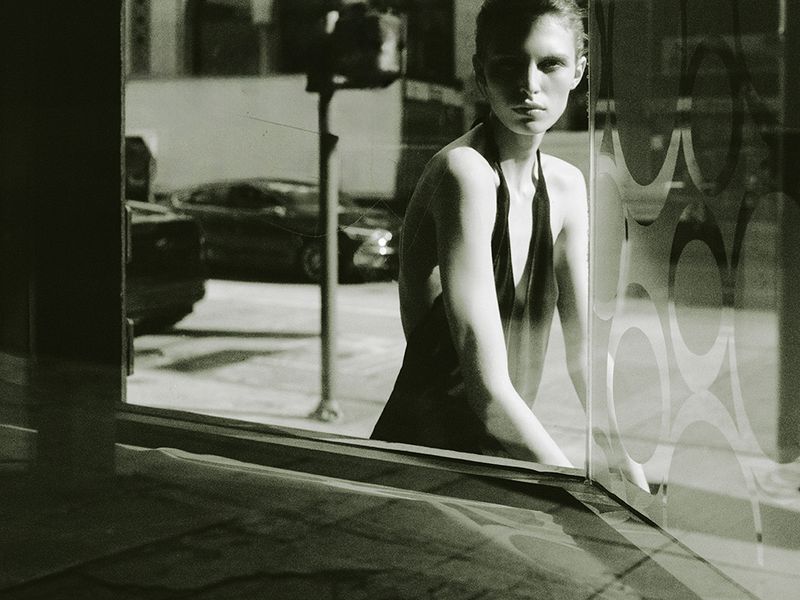 Model wearing a dark halter top standing near a patterned glass window with a night street background for Zara