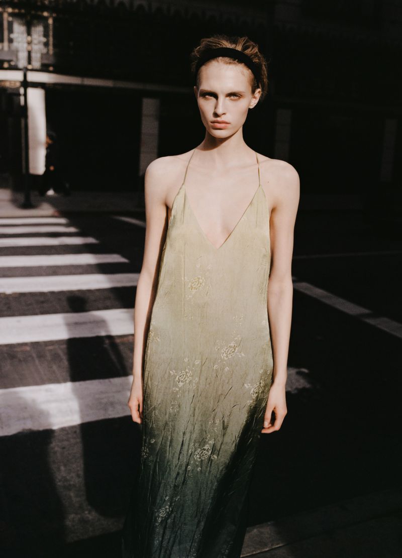 Model standing outdoors wearing a long ombre slip dress with thin straps and a headband in daylight
