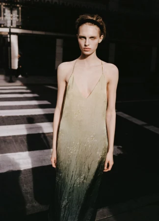 Model standing outdoors wearing a long ombre slip dress with thin straps and a headband in daylight