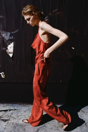 Model in a red silk top and matching trousers walking against a dark poster-covered wall for Zara