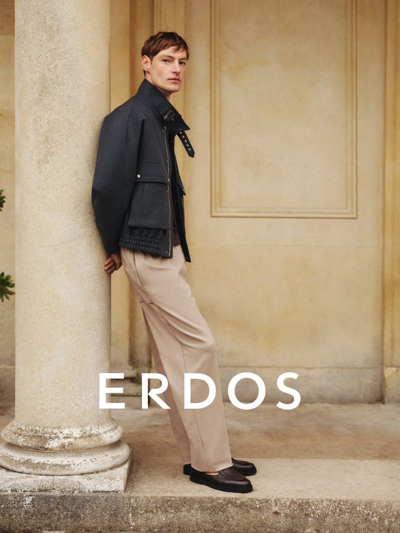 Male model leaning against a stone column wearing a dark jacket and beige trousers for the Erdos Spring Summer 2026 campaign.