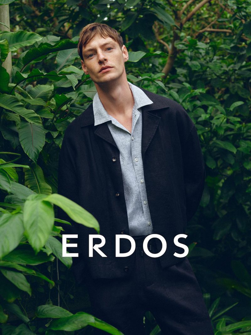 Male model wearing a dark jacket over a light polo shirt amidst lush green foliage for Erdos Spring Summer 2026.