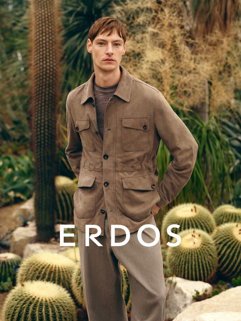 Male model wearing a taupe button-up jacket and trousers, standing among cacti and desert vegetation.
