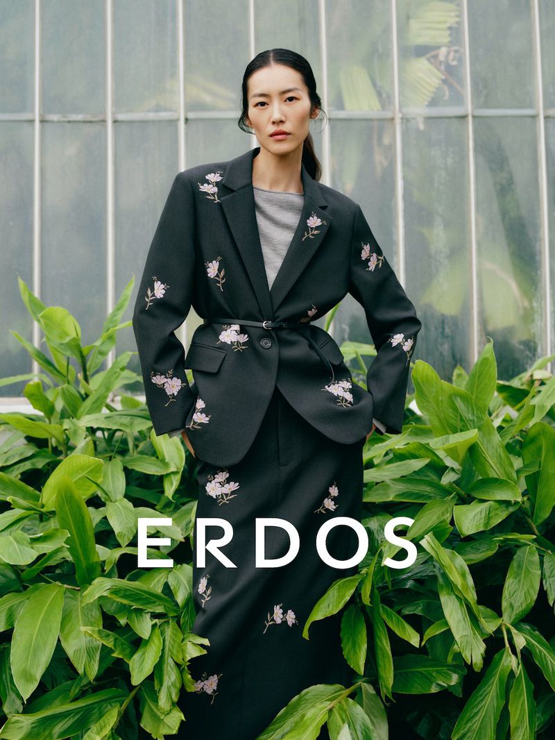 Model Liu Wen wearing a dark floral embroidered blazer and matching skirt against a greenhouse background for Erdos Spring Summer 2026