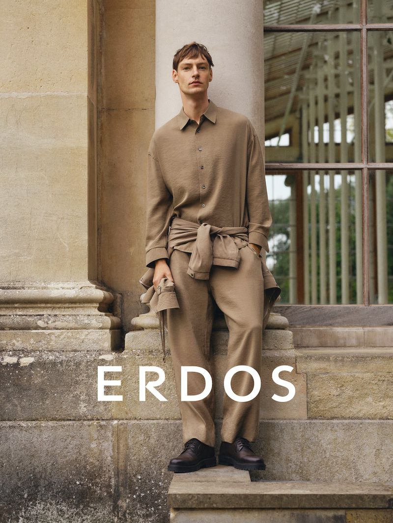 A male model leaning against a stone column wearing a tan button-down shirt and matching trousers for Erdos.