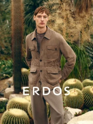 Male model wearing a taupe button-up jacket and trousers, standing among cacti and desert vegetation.