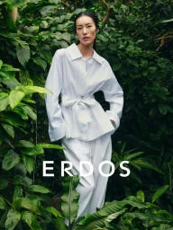 Model Liu Wen wearing a white buttoned shirt and matching trousers standing amidst lush tropical foliage for Erdos Spring Summer 2026.