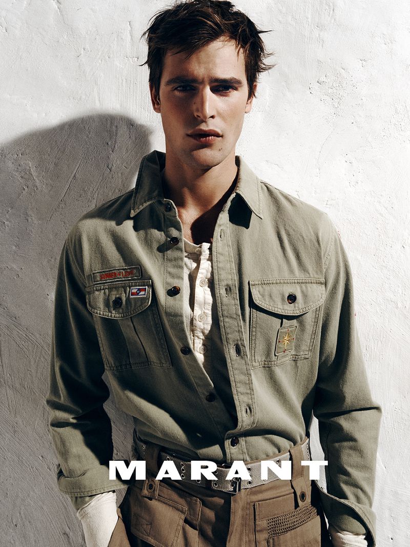Parker Van Noord wearing an olive green utility shirt and tan trousers against a textured white wall for Isabel Marant.
