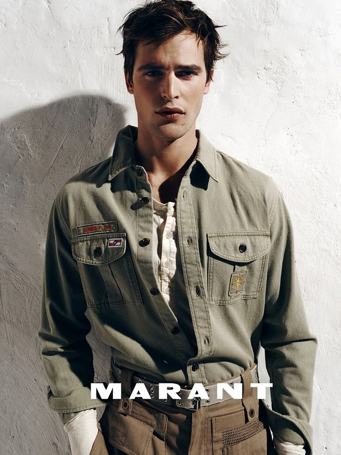 Parker Van Noord wearing an olive green utility shirt and tan trousers against a textured white wall for Isabel Marant.