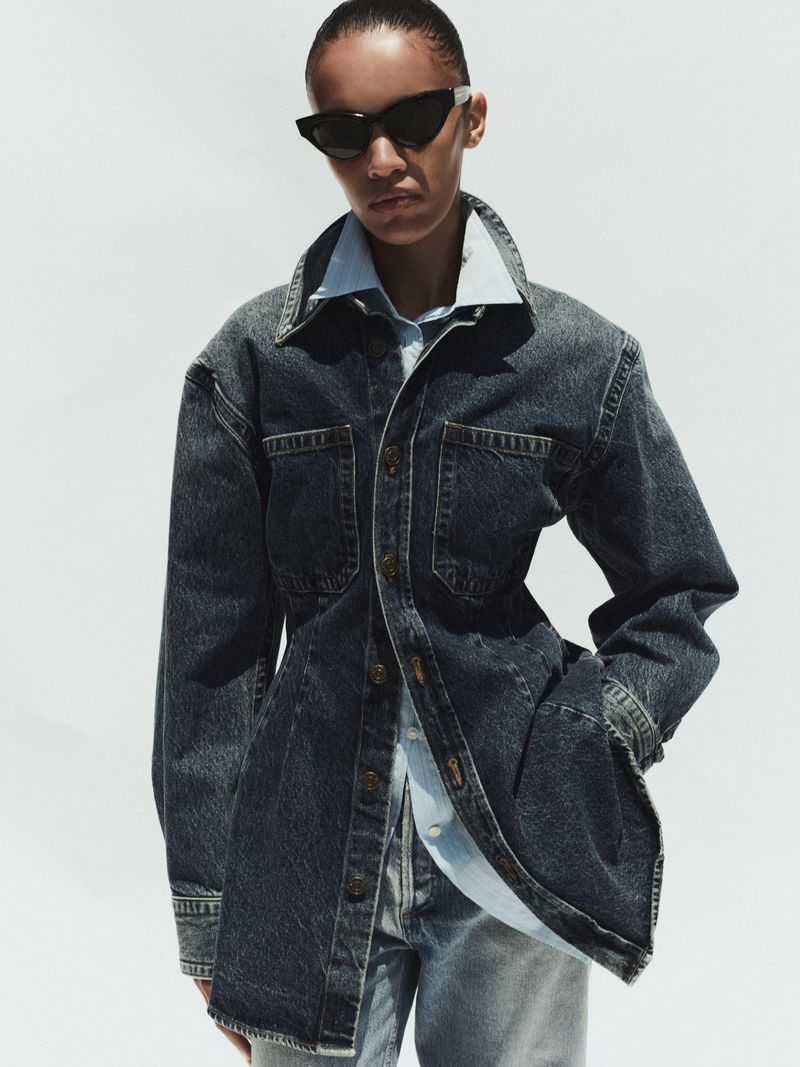 Model wearing a dark denim jacket and sunglasses against a bright white background for Agolde Spring 2026.