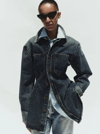Model wearing a dark denim jacket and sunglasses against a bright white background for Agolde Spring 2026.