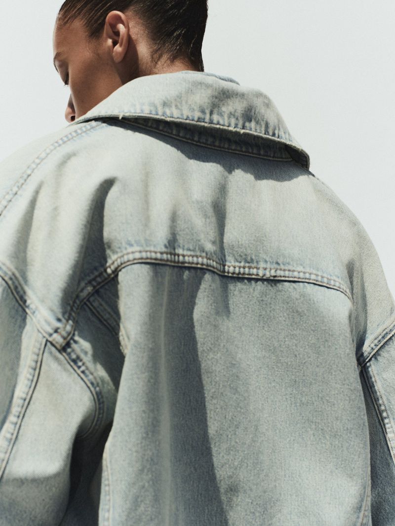 Close-up portrait of a model wearing an oversized light blue denim jacket against a bright white background.