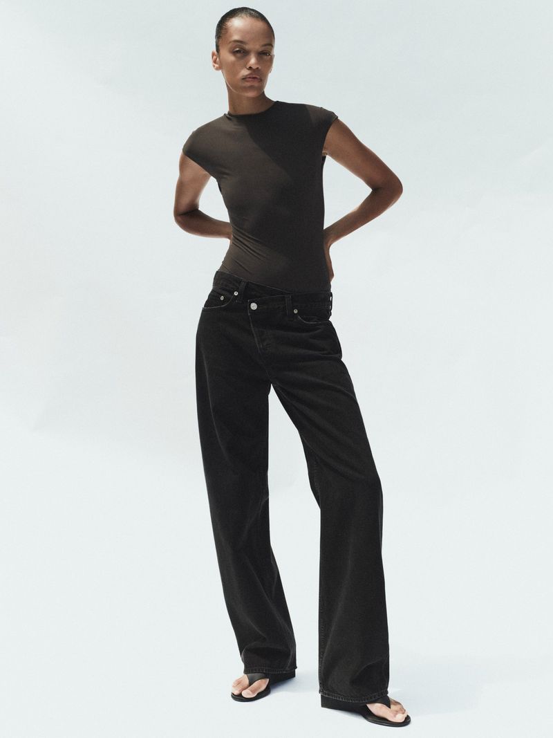 Model Kukua Williams wearing black jeans and a dark t-shirt against a white studio background for Agolde Spring 2026.