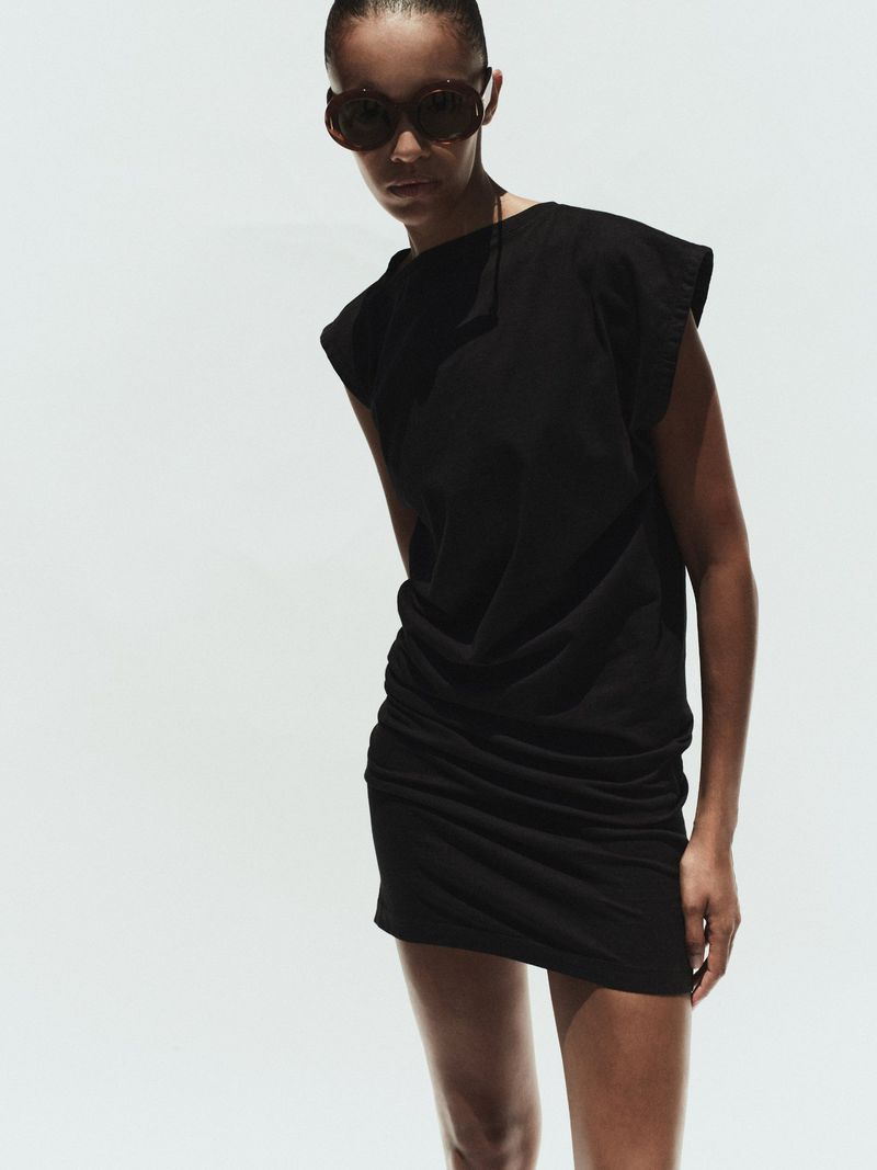 Model wearing a black dress and dark sunglasses against a bright white background for AGOLDE Spring 2026.