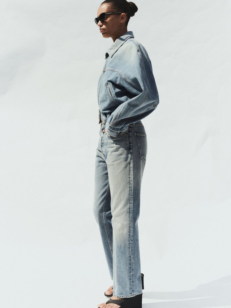 Model in denim jacket and jeans wearing sunglasses against a white background for AGOLDE Spring 2026