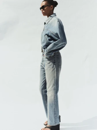 Model in denim jacket and jeans wearing sunglasses against a white background for AGOLDE Spring 2026