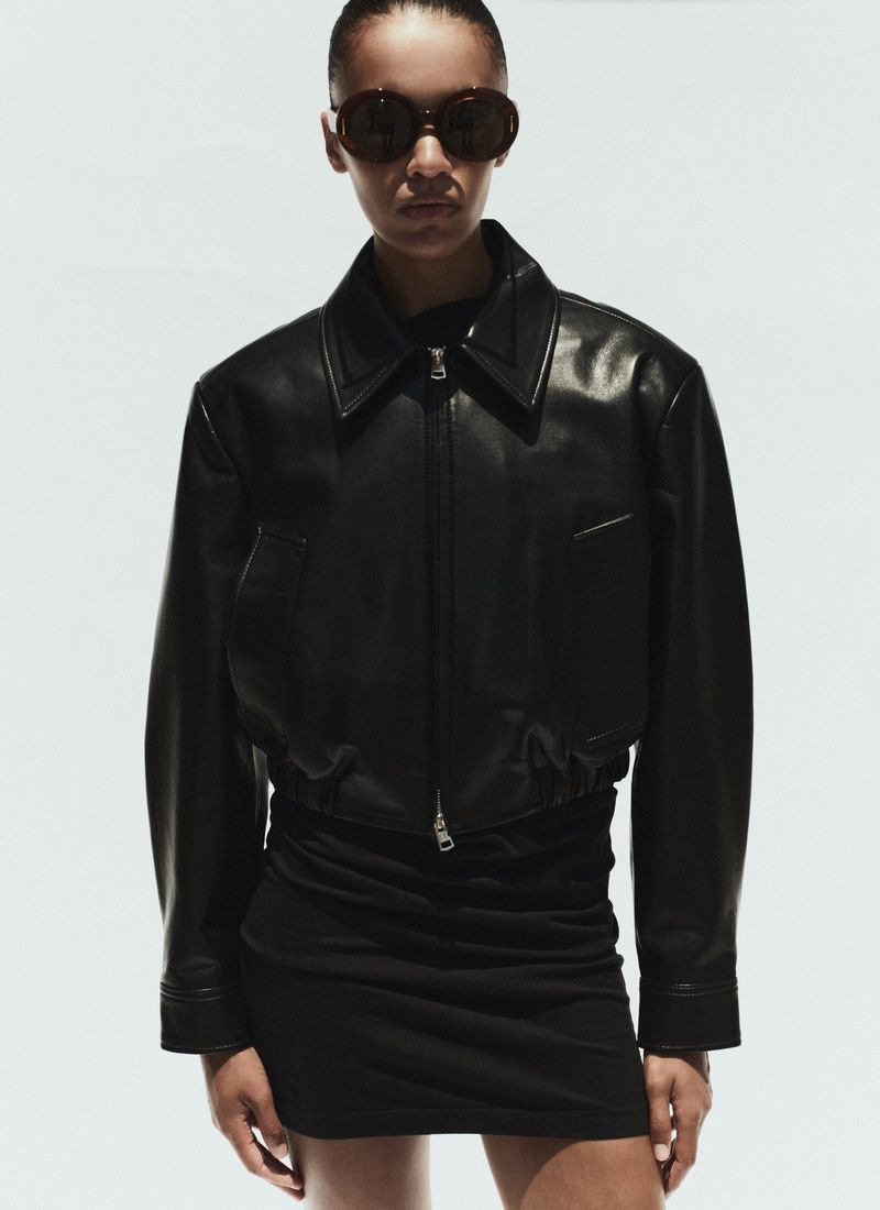 Model wearing a black leather jacket and sunglasses against a seamless white background for AGOLDE Spring 2026.