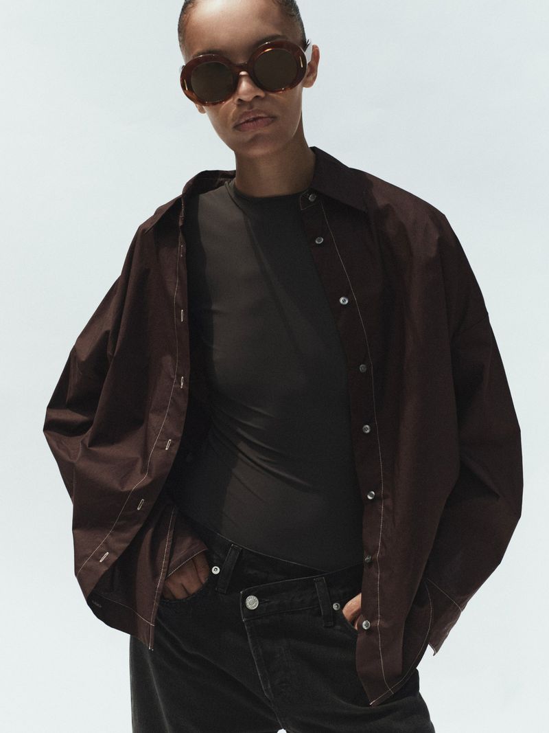 Model wearing dark oversized shirt and sunglasses against a plain light background for Agolde Spring 2026