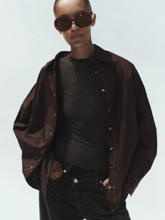 Model wearing dark oversized shirt and sunglasses against a plain light background for Agolde Spring 2026