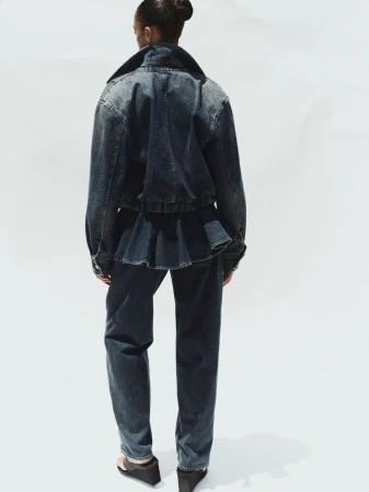Model wearing dark denim jacket and matching jeans seen from behind against a plain white studio background.