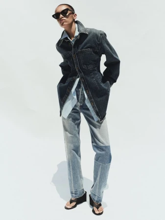 Model in dark sunglasses wearing a denim jacket and jeans against a white seamless background