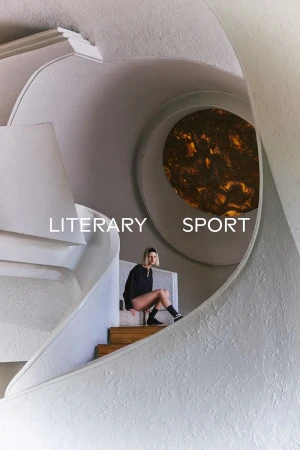 Model seated on a wooden staircase inside an architectural interior with curved white walls and a glowing circular window.