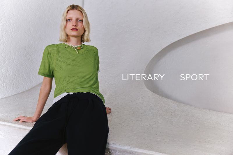 Model wearing a green mesh t-shirt and black trousers seated on a white textured architectural curve with text reading LITERARY SPORT