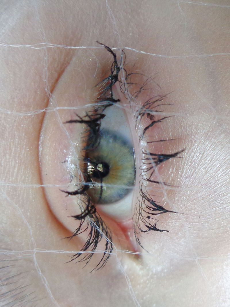 Close-up of a blue and green eye with black lashes, viewed through a fine white net, creating an artistic and slightly obscured view.