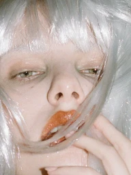 Close-up portrait of a model with silver white hair and glossy lips holding strands across her face for METAL Magazine.