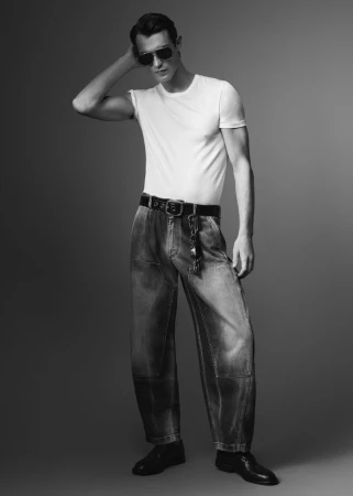 Monochrome fashion portrait of a male model wearing a white t-shirt and denim jeans against a grey seamless studio background.