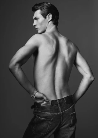 Shirtless male model wearing dark denim jeans posing against a grey studio backdrop for Dolce & Gabbana