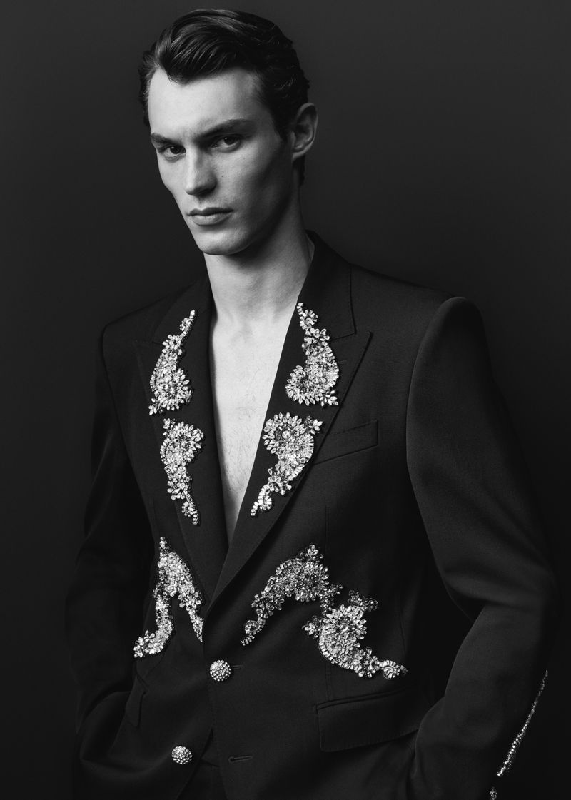 Monochrome portrait of a male model wearing an embroidered blazer against a dark background