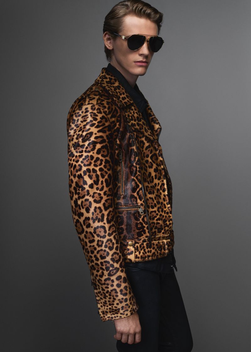 A male model wearing a leopard print jacket and dark sunglasses against a neutral grey studio background.