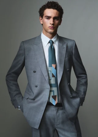 Model in a grey double-breasted suit and patterned teal tie against a neutral grey studio background