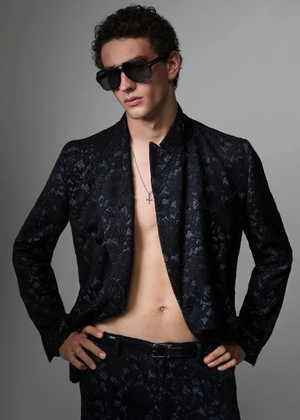 Male model wearing dark sunglasses and a black patterned blazer against a neutral grey studio background