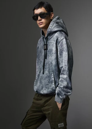Model wearing dark sunglasses, grey acid-wash hoodie, and dark cargo trousers against a neutral studio backdrop