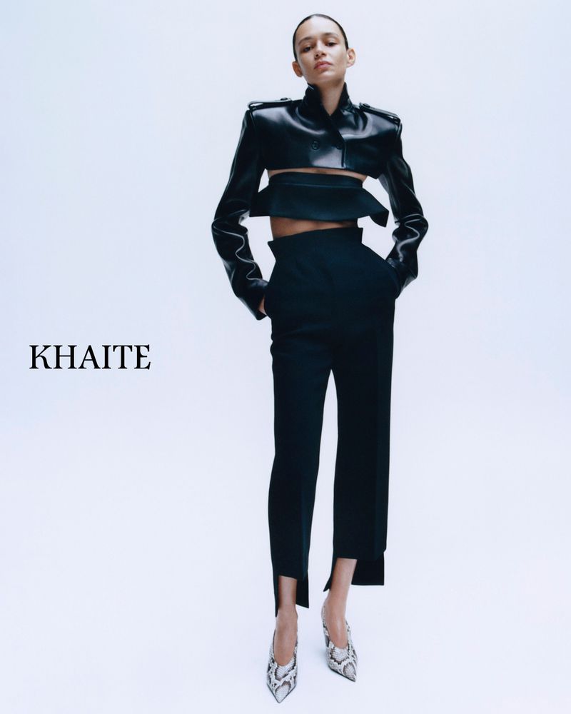 Model wearing a cropped black leather jacket and black trousers against a white seamless background